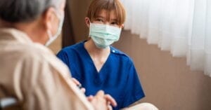 a masked health care worker chatting with an elderly person