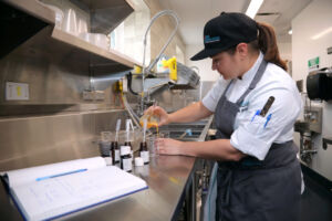 Chef taking precise measurements in kitchen with notebook and pen beside her.