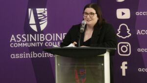 Jana Sproule, Chairperson of Media and Office Technology at Assiniboine, standing at podium with Assiniboine Community College branding in the background